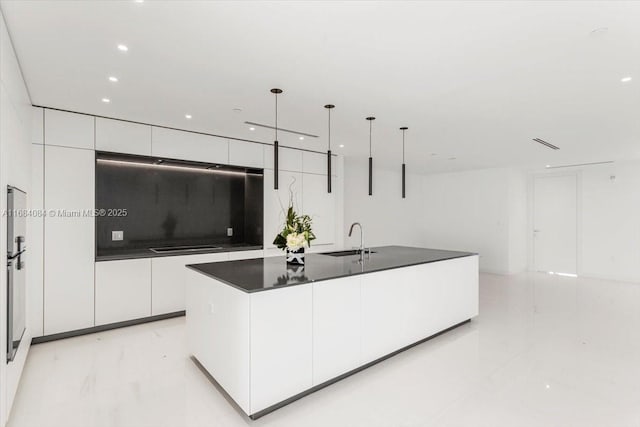 kitchen with pendant lighting, dark countertops, white cabinetry, an island with sink, and modern cabinets