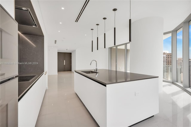 kitchen with white cabinets, a center island with sink, sink, a wall of windows, and decorative light fixtures