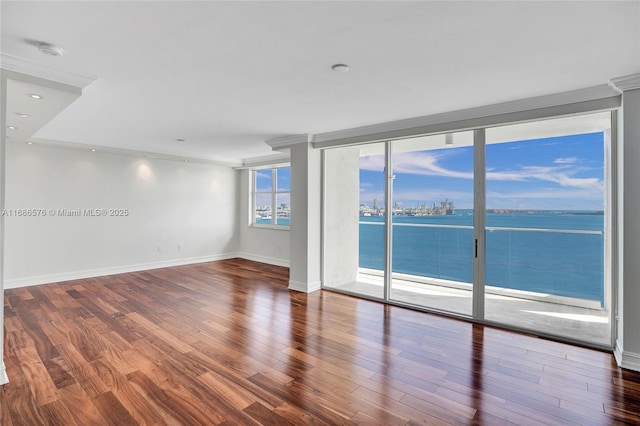 spare room with expansive windows, a water view, wood finished floors, and baseboards