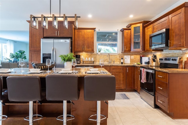 kitchen with a breakfast bar area, hanging light fixtures, stainless steel appliances, a center island, and light stone counters