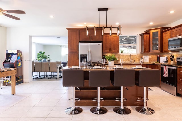 kitchen featuring a center island, pendant lighting, appliances with stainless steel finishes, light stone counters, and ceiling fan