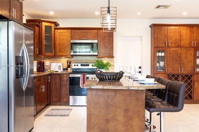 kitchen featuring decorative backsplash, a kitchen breakfast bar, light stone countertops, pendant lighting, and stainless steel appliances