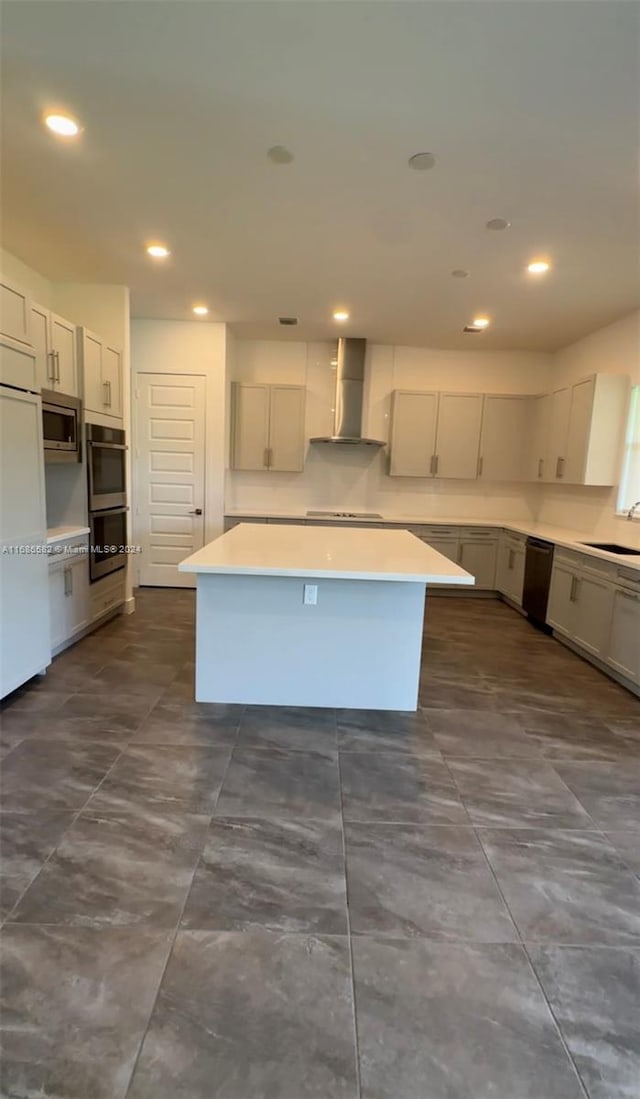 kitchen with sink, a kitchen island, appliances with stainless steel finishes, and wall chimney range hood