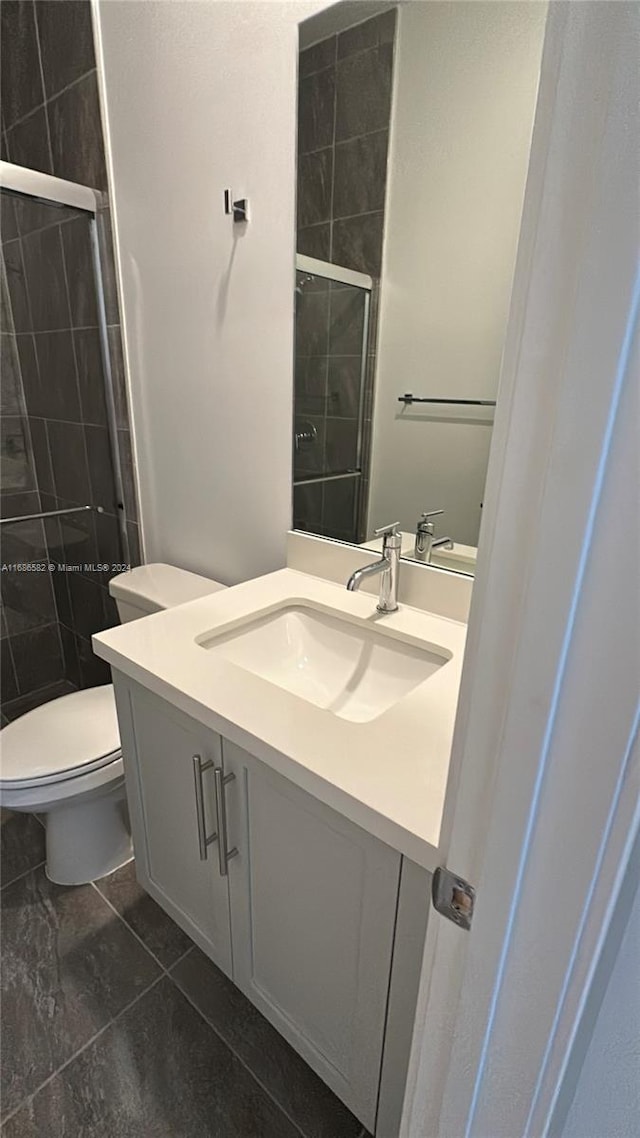 bathroom with vanity, toilet, a shower with shower door, and tile patterned flooring