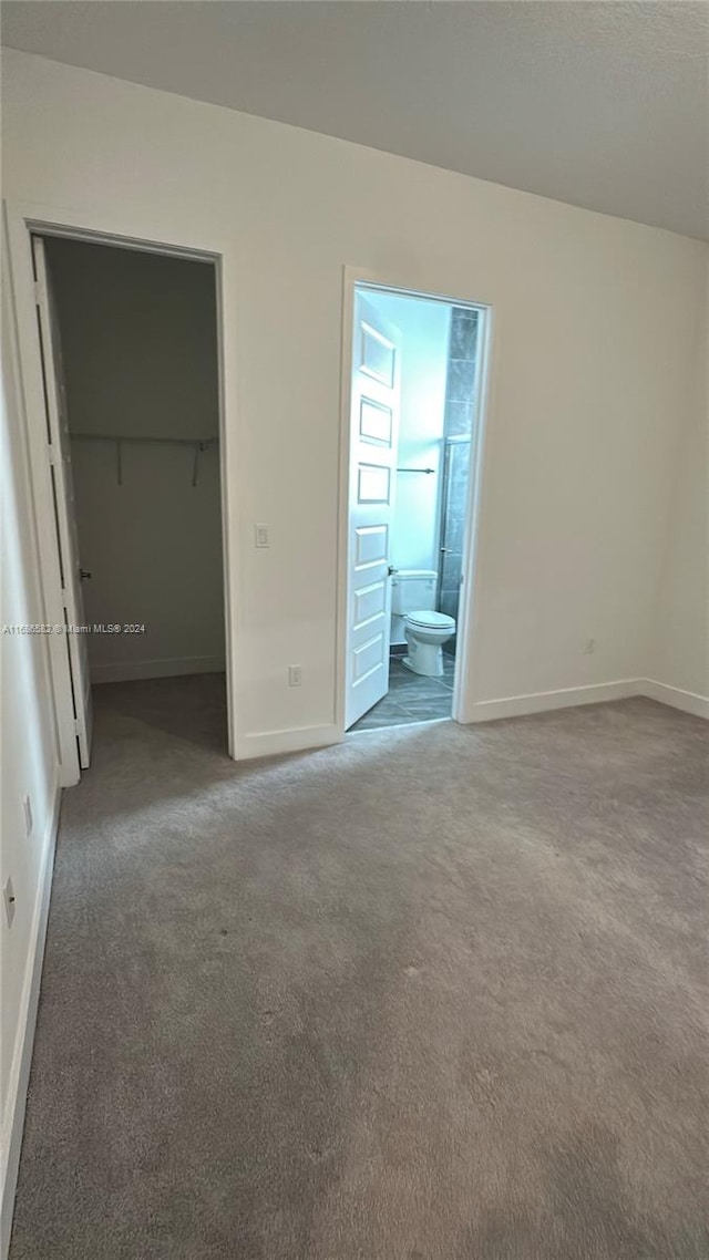 unfurnished bedroom featuring a closet, ensuite bathroom, a spacious closet, and dark colored carpet