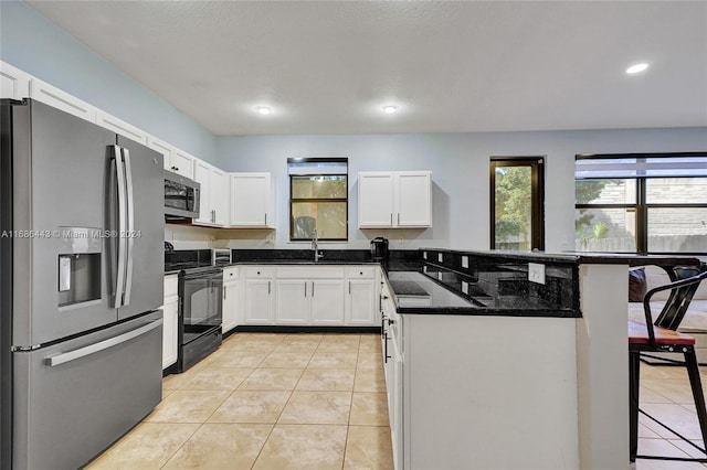 kitchen with a breakfast bar area, dark stone counters, white cabinets, light tile patterned floors, and appliances with stainless steel finishes