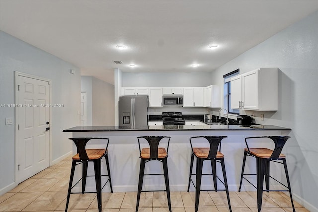 kitchen with sink, a breakfast bar, white cabinets, light tile patterned floors, and appliances with stainless steel finishes