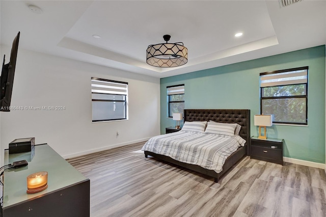 bedroom with light hardwood / wood-style floors and a tray ceiling