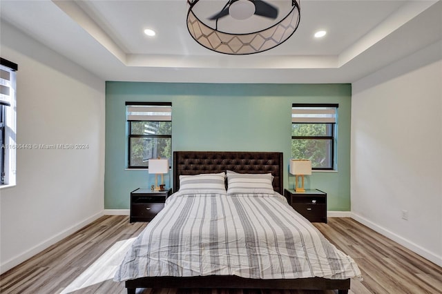 bedroom with light hardwood / wood-style floors, a tray ceiling, and multiple windows