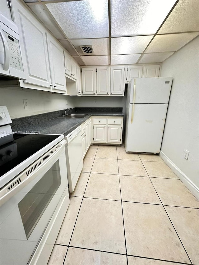 kitchen with white appliances, light tile patterned flooring, a drop ceiling, and white cabinets