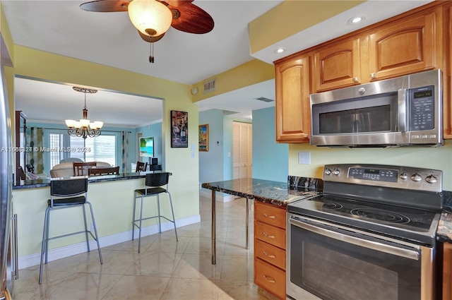 kitchen featuring appliances with stainless steel finishes, ceiling fan with notable chandelier, dark stone counters, decorative light fixtures, and a breakfast bar