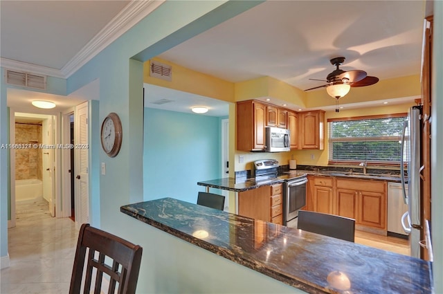 kitchen with kitchen peninsula, ceiling fan, dark stone countertops, crown molding, and stainless steel appliances