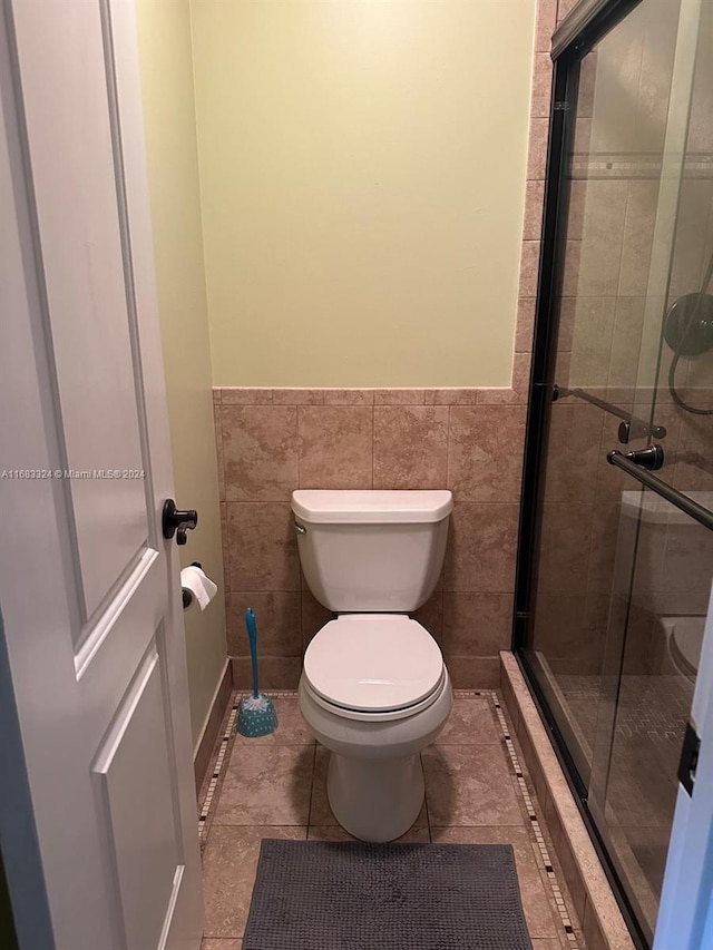 bathroom featuring toilet, walk in shower, tile patterned floors, and tile walls