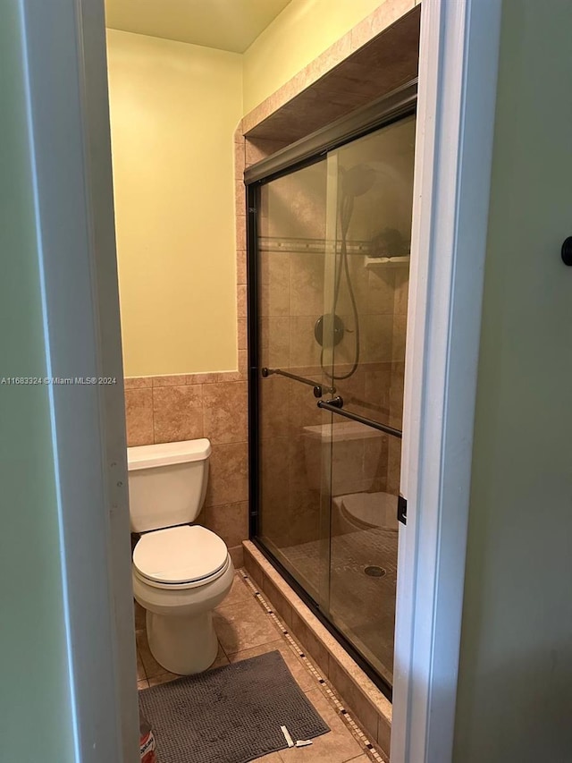 bathroom featuring toilet, walk in shower, tile patterned flooring, and tile walls