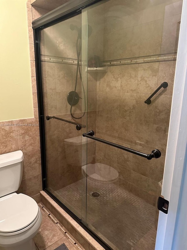 bathroom featuring toilet, tile patterned floors, tile walls, and a shower with shower door