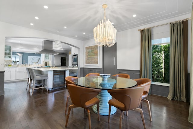 dining space featuring dark wood-type flooring, crown molding, an inviting chandelier, and beverage cooler