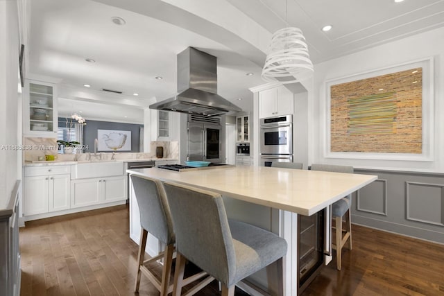 kitchen featuring white cabinetry, decorative light fixtures, a kitchen bar, and island range hood