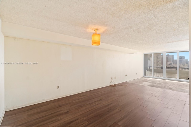 empty room featuring a wall of windows, wood-type flooring, and a textured ceiling