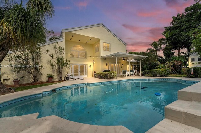 pool at dusk with french doors, a patio, and ceiling fan