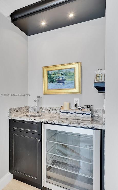 bar with light stone countertops, sink, and beverage cooler