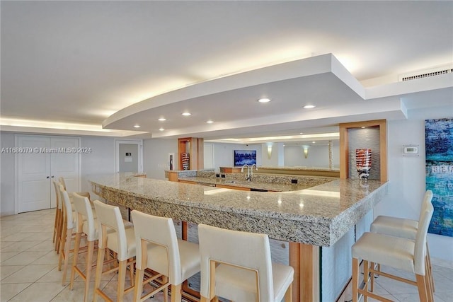 kitchen featuring sink, light stone counters, kitchen peninsula, a breakfast bar, and light tile patterned floors