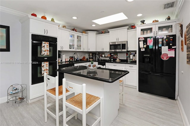 kitchen with white cabinets, a kitchen island, backsplash, a kitchen bar, and black appliances