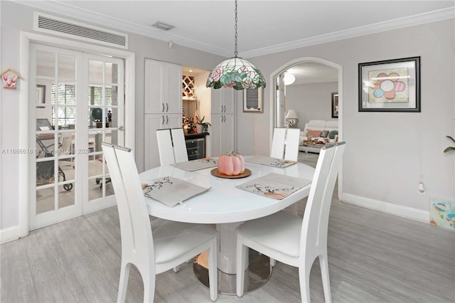 dining room with french doors, ornamental molding, and light wood-type flooring