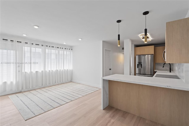 kitchen with light brown cabinets, stainless steel fridge, kitchen peninsula, hanging light fixtures, and light hardwood / wood-style floors