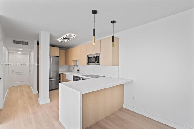 kitchen featuring light brown cabinetry, appliances with stainless steel finishes, light wood-type flooring, kitchen peninsula, and decorative light fixtures