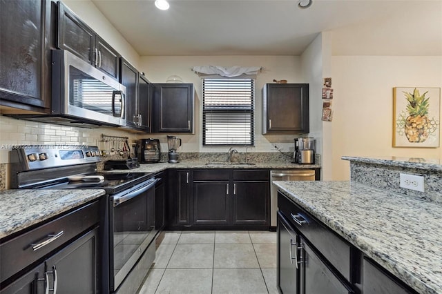 kitchen with sink, tasteful backsplash, light stone counters, light tile patterned flooring, and appliances with stainless steel finishes