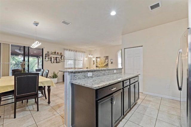 kitchen with decorative light fixtures, light stone counters, light tile patterned floors, and stainless steel refrigerator