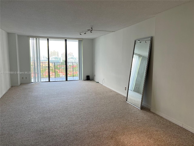 carpeted empty room featuring track lighting, a textured ceiling, ceiling fan, and floor to ceiling windows