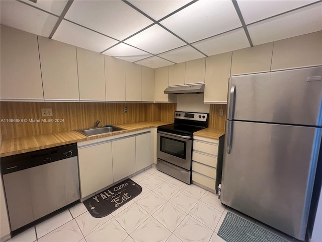 kitchen with cream cabinets, stainless steel appliances, a paneled ceiling, light tile patterned floors, and sink