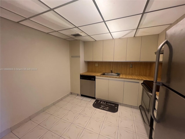 kitchen featuring a paneled ceiling, appliances with stainless steel finishes, sink, and cream cabinetry