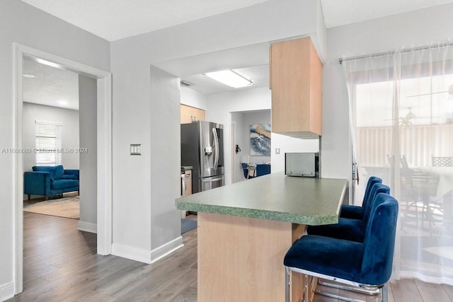 kitchen featuring kitchen peninsula, hardwood / wood-style floors, stainless steel fridge with ice dispenser, a kitchen bar, and a textured ceiling