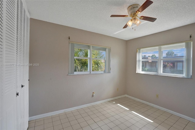 empty room with ceiling fan, light tile patterned floors, and a textured ceiling