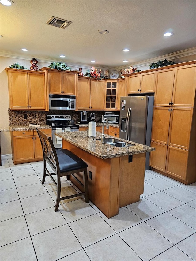 kitchen with crown molding, a kitchen island with sink, a kitchen breakfast bar, stainless steel appliances, and dark stone counters