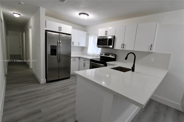 kitchen with appliances with stainless steel finishes, white cabinets, sink, and kitchen peninsula