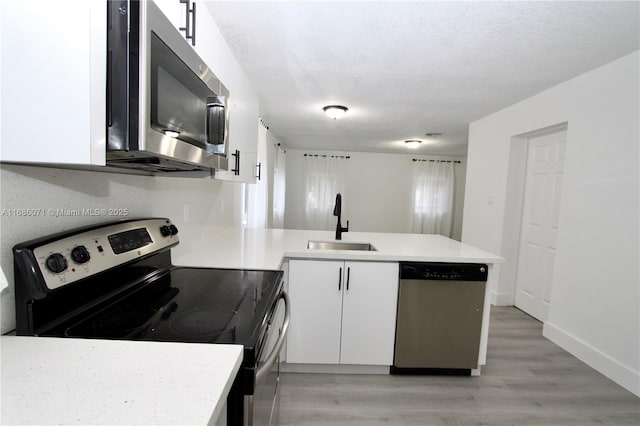 kitchen with sink, white cabinetry, light hardwood / wood-style flooring, kitchen peninsula, and appliances with stainless steel finishes