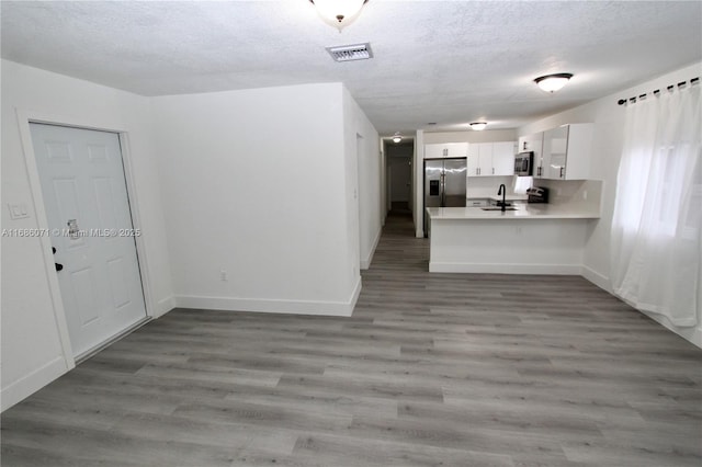 kitchen with stainless steel appliances, a textured ceiling, white cabinetry, hardwood / wood-style flooring, and kitchen peninsula