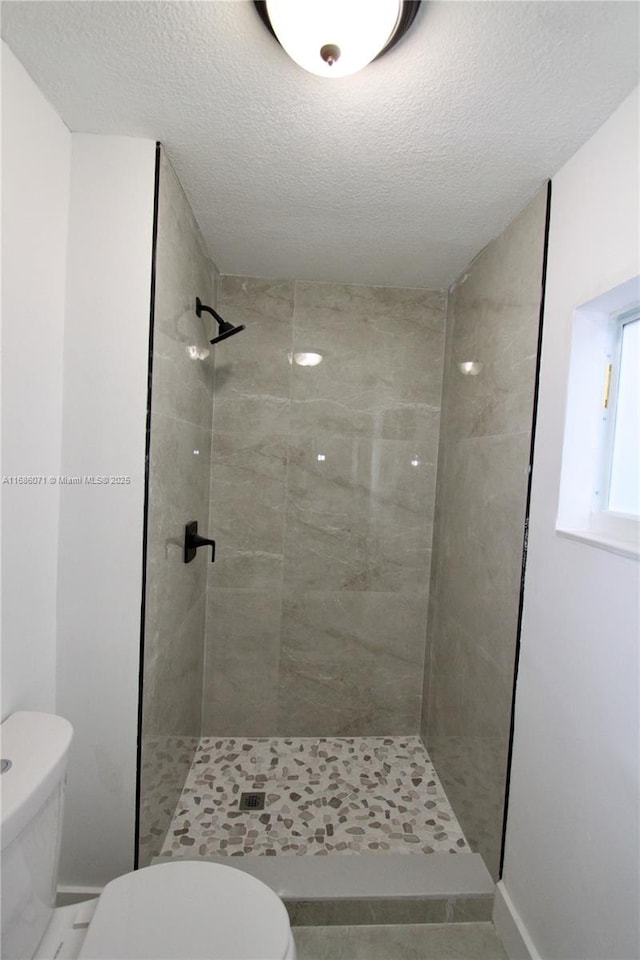 bathroom with a textured ceiling, a tile shower, and toilet