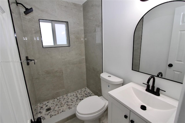 bathroom featuring toilet, a tile shower, and vanity