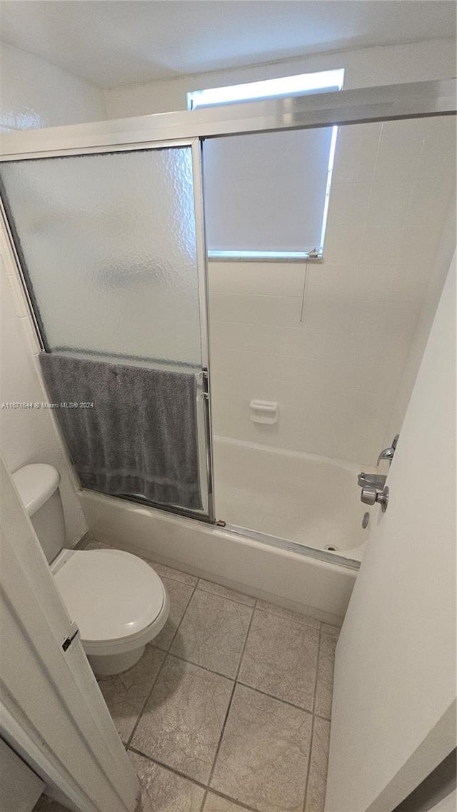 bathroom with tile patterned floors, bath / shower combo with glass door, and toilet