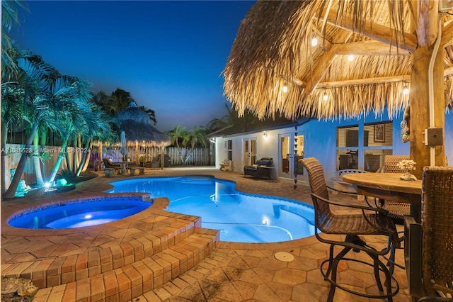 pool at dusk featuring an in ground hot tub and a patio