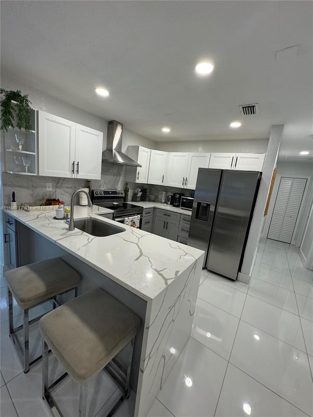 kitchen featuring white cabinetry, appliances with stainless steel finishes, wall chimney exhaust hood, and kitchen peninsula