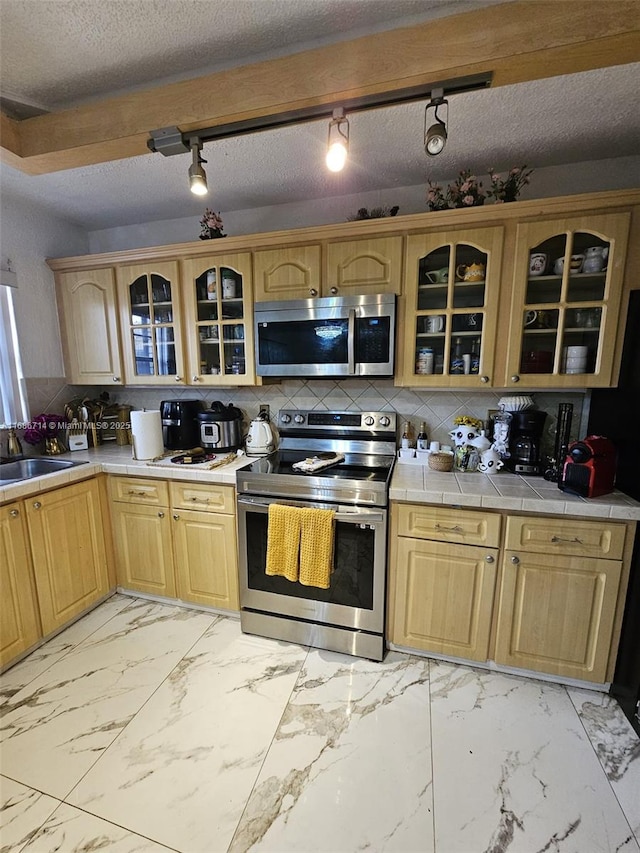 kitchen featuring tile countertops, sink, decorative backsplash, a textured ceiling, and appliances with stainless steel finishes