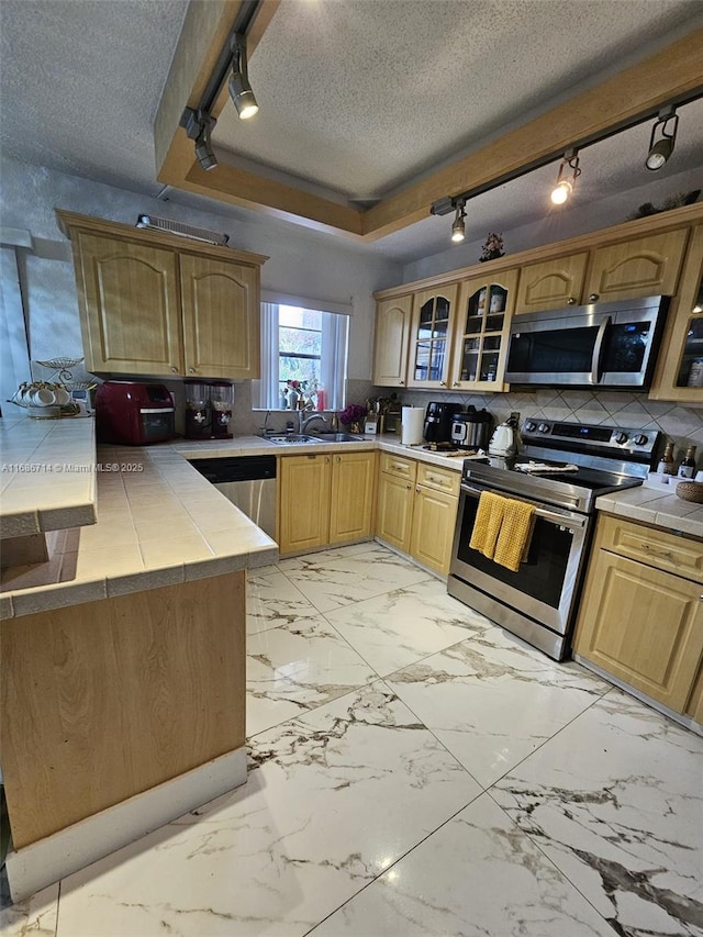 kitchen featuring backsplash, a textured ceiling, stainless steel appliances, sink, and tile countertops