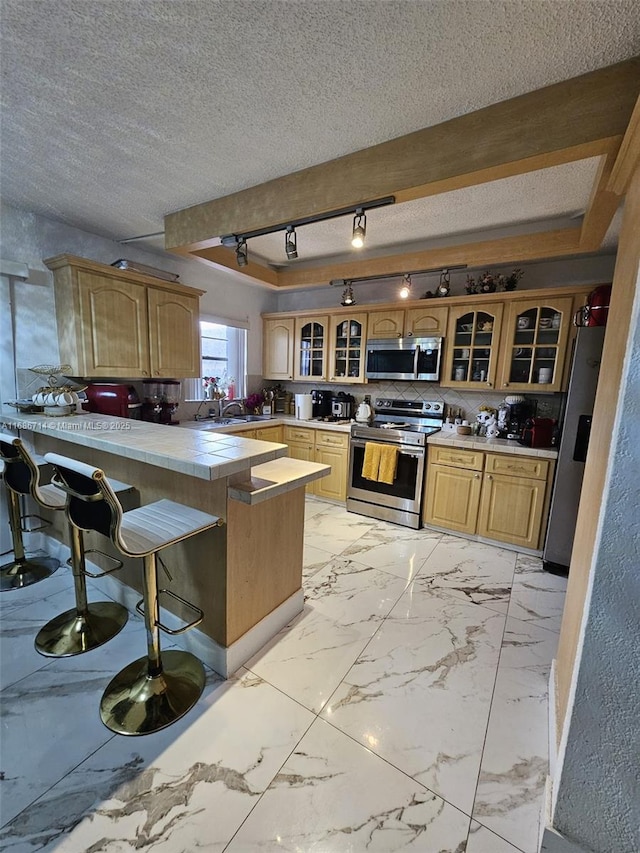 kitchen with tile counters, stainless steel appliances, kitchen peninsula, a textured ceiling, and a breakfast bar area