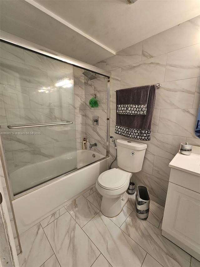 full bathroom featuring vanity, bath / shower combo with glass door, tile walls, and toilet