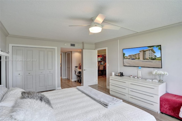 bedroom with ceiling fan, a textured ceiling, ornamental molding, light hardwood / wood-style floors, and a closet